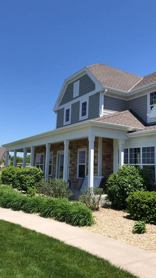 Blue-gray cedar lap and shake siding with white trim on a stone-front home