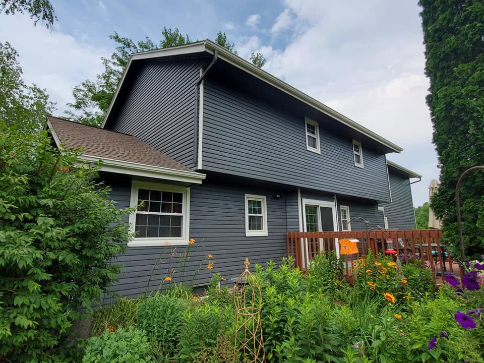 Side view of a home with dark blue-gray vinyl siding beside a raised deck