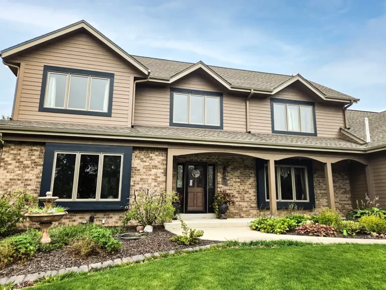 Two-story home with tan lap siding, dark blue window trim and a brick front porch