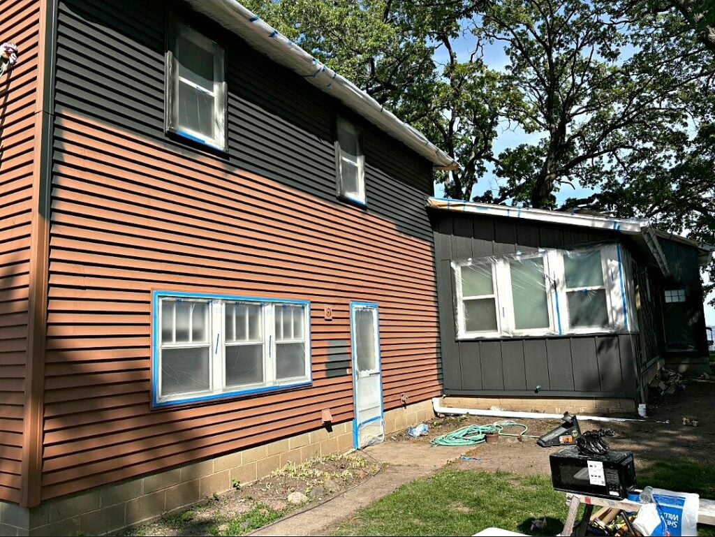 West Bend home with brown siding before the dark repaint, windows masked for prep