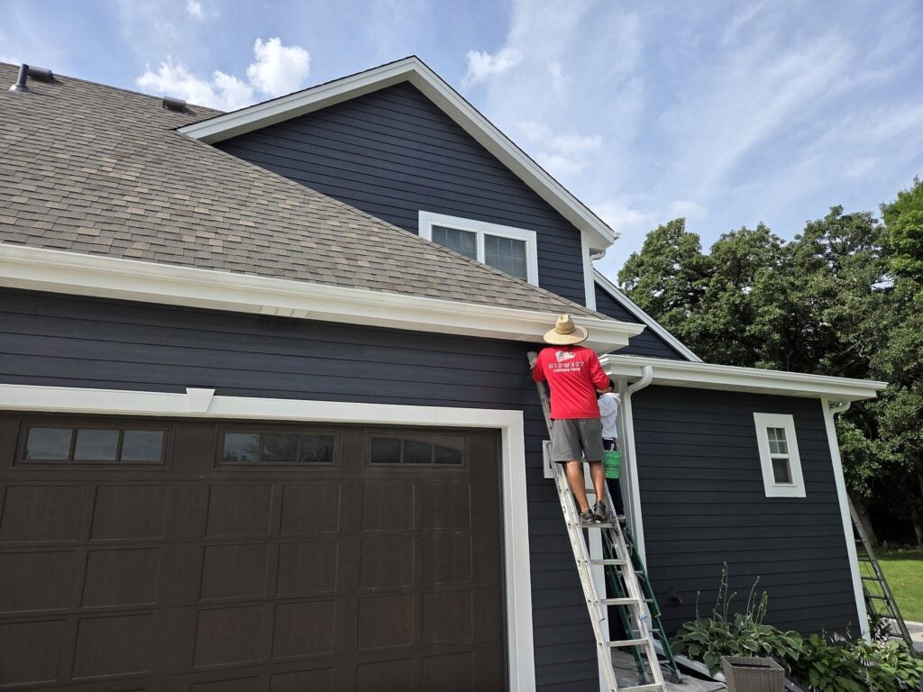 Painter on a ladder painting white trim on a blue-gray house in Mukwonago