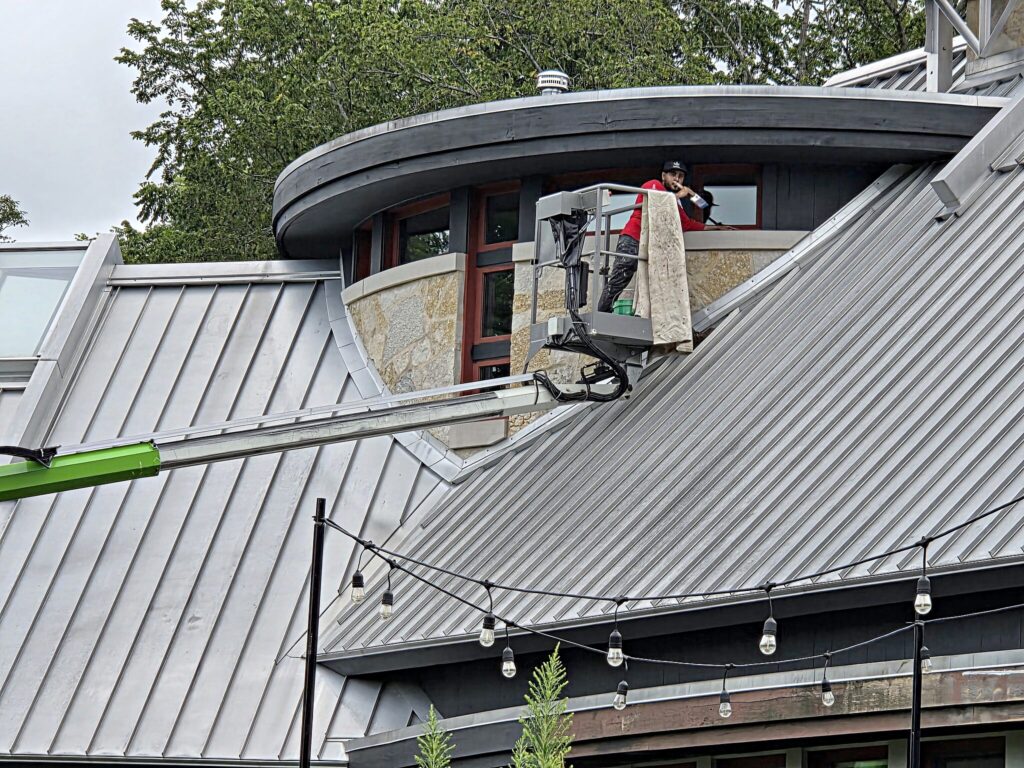 Painter in a lift working on a curved stone tower with metal roofing in Mukwonago